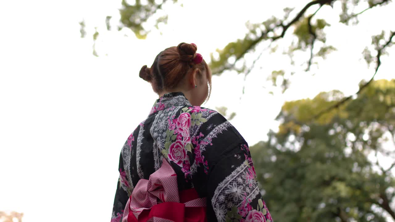Một người phụ nữ mặc yukata họa tiết hoa đi qua một khu rừng tươi tốt tại một đền thờ Thần đạo.