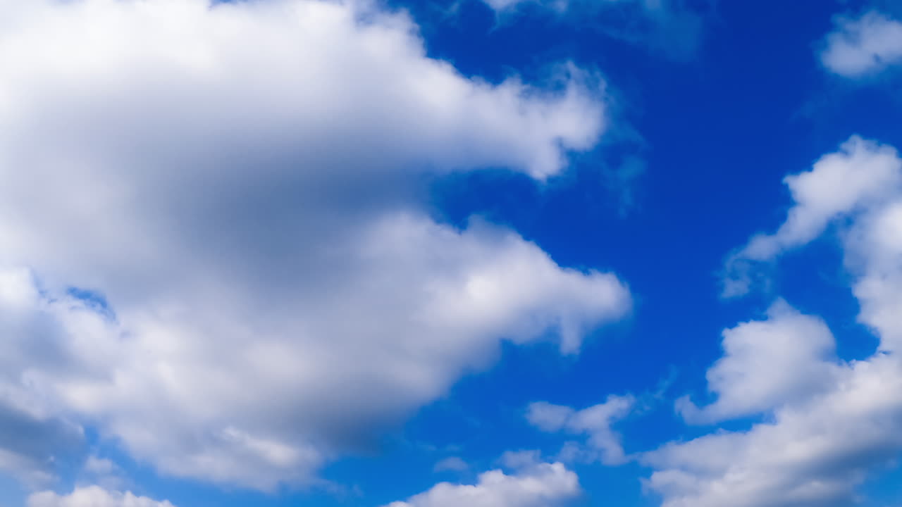 White cotton clouds in the blue sky. Wind blowing the cloudscape by the horizon. Low angle view. Timelapse.