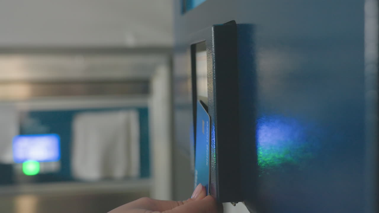 Round view of cashless payment panel on wall as customer hand taps card on reader then removes it, contactless transaction under blue light, glossy reflection, modern laundromat machine detail