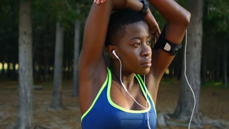 female athlete performing stretching exercise while listening music in forest 4k