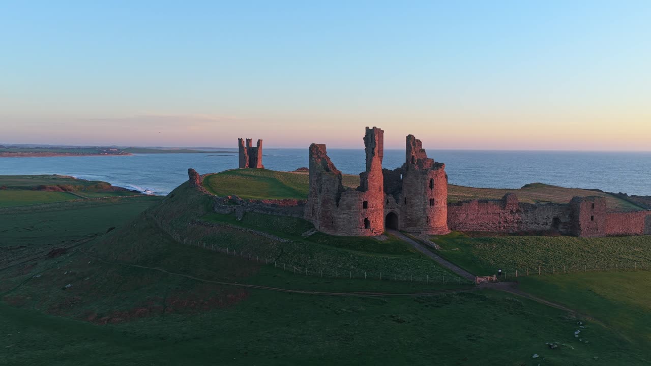 Dunstanburgh slotsruiner gløder ved solopgang ved kysten