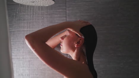 mujer desnuda ajusta el cabello en la cabina de ducha. señora tranquila acaricia la cabeza lavando el cuerpo en el baño de casa elegante. mujer descansa en puros chorros húmedos en el salón