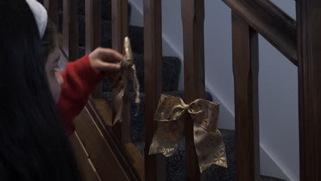 young girl teenager sticking double christmas bows with gold leaf design on stair spindles