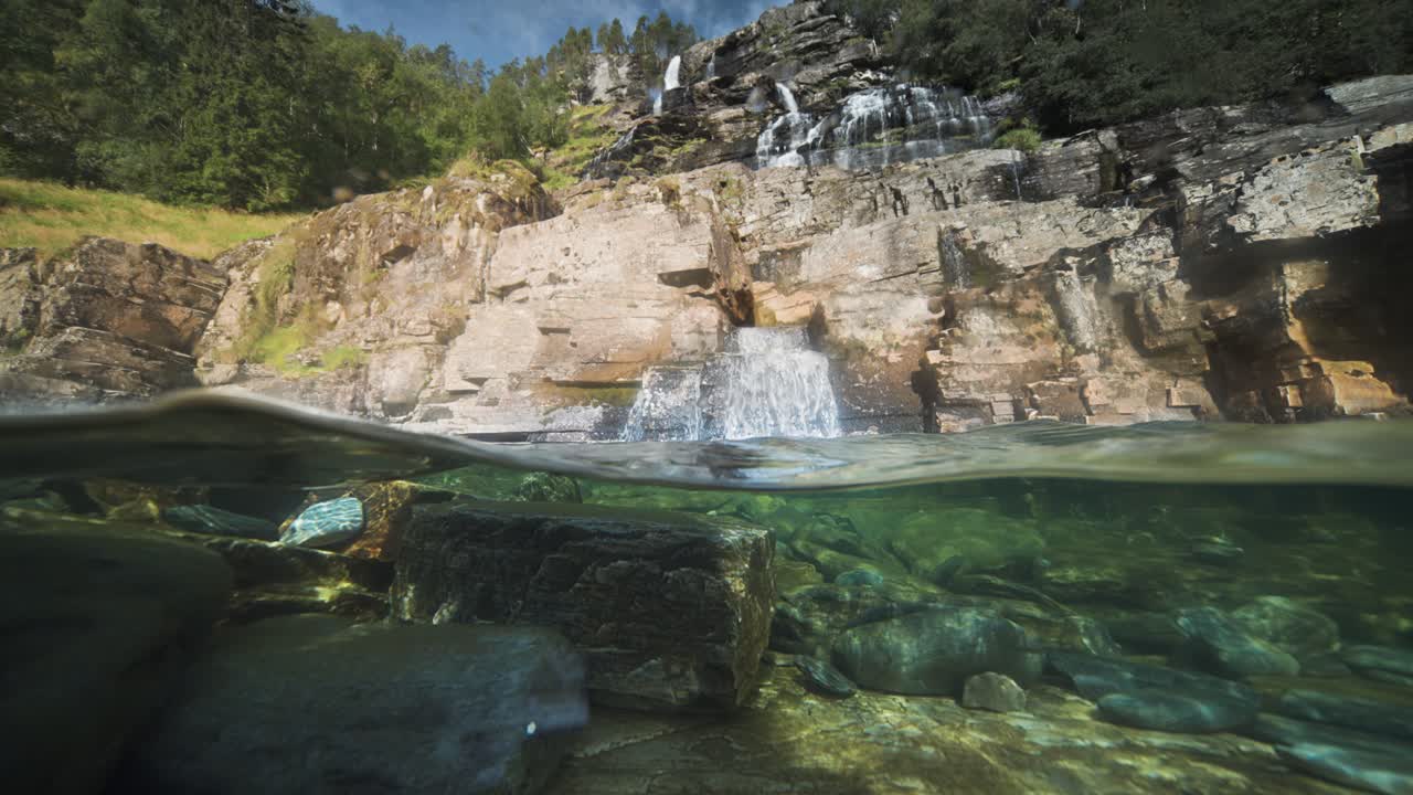 vista relajante de un río poco profundo con orillas rocosas y aguas transparentes, con una cascada en el fondo