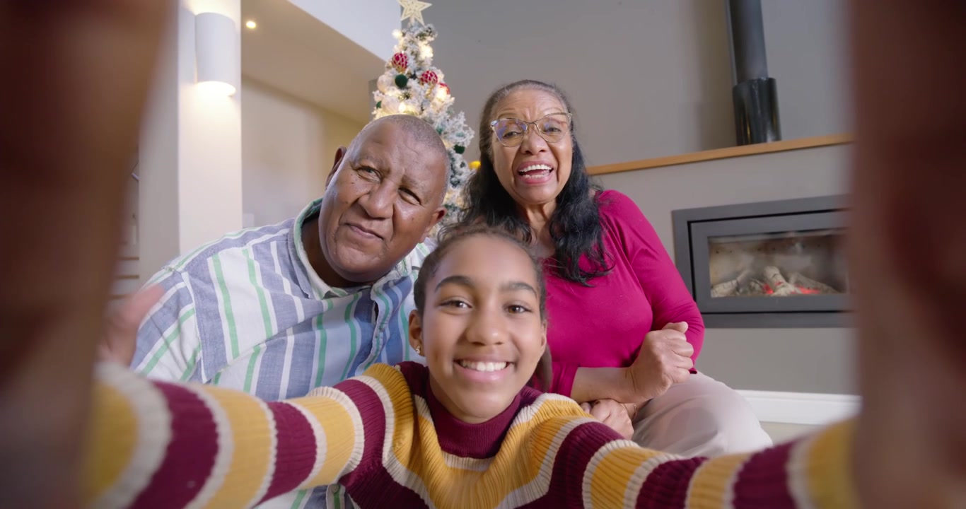 African American family positioning phone for selfie, waving, smiling by Christmas tree