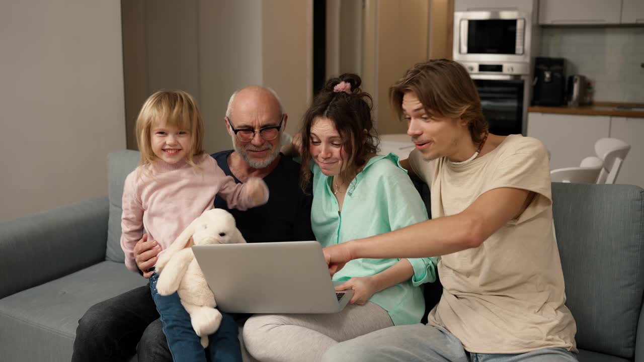 los niños y el abuelo están riendo juntos mientras usan una computadora portátil, viendo video