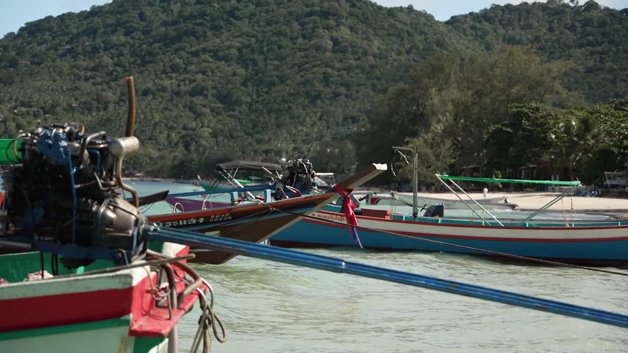 Empty wooden longtail boats are moored in the clear shallow waters of Koh Tao, Thailand, surrounded by lush green hills and sandy beaches, creating a serene and picturesque scene