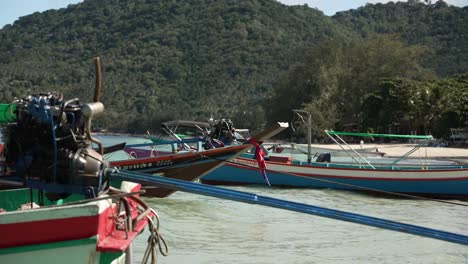 los barcos de cola larga de madera vacíos están amarrados en las aguas claras y poco profundas de koh tao, tailandia, rodeados de exuberantes colinas verdes y playas de arena, creando una escena serena y pintoresca.