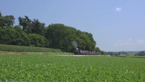 Una-Máquina-De-Vapor-De-1924-Con-Un-Tren-De-Pasajeros-Que-Echa-Humo-Y-Viaja-A-Lo-Largo-De-La-Campiña-Amish-En-Un-Día-De-Verano