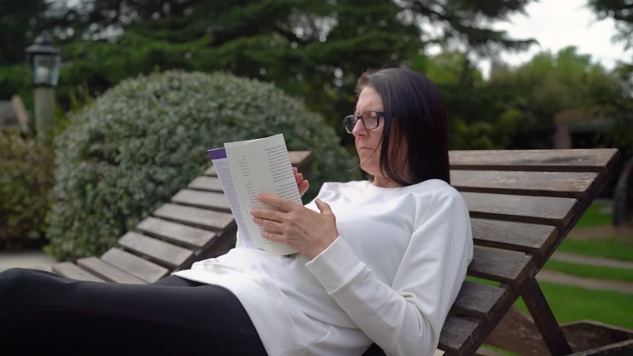 mujer solitaria en una silla de descanso leyendo un libro al aire libre