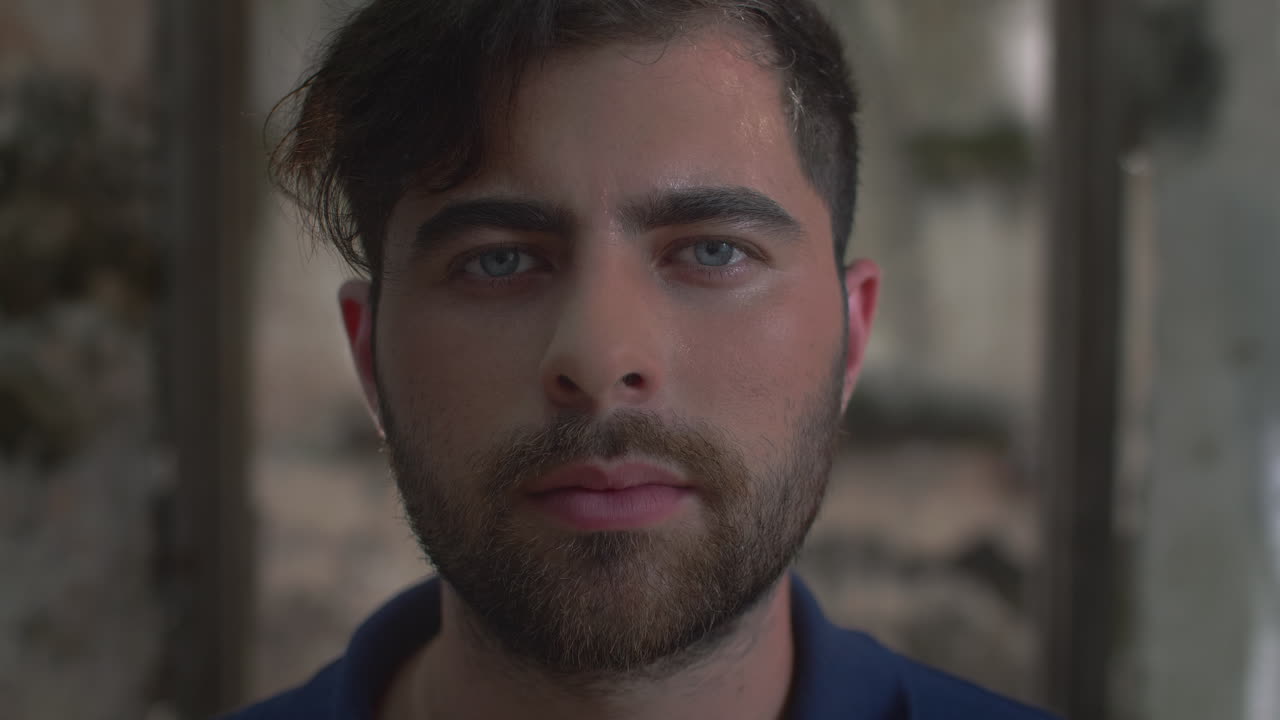 High-quality 4K footage of a focused young man with blue eyes and a beard, slowly opening his eyes in a cinematic outdoor setting. Ideal for travel, identity, mystery, or emotional