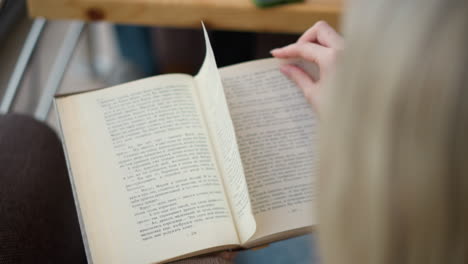 close-up of lady hand gliding over book pages as she tries to turn to a new page while another page folds back, wooden table with phone visible in blurred background