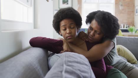 sad african american mother and daughter sitting on sofa, embracing