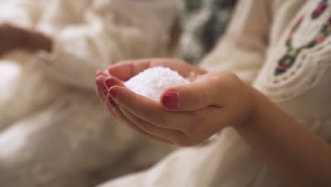 Toma-En-Cámara-Lenta-De-Dos-Niños-Vestidos-Con-Vestidos-Blancos-Adornados-De-Navidad-Sosteniendo-Nieve-Falsa-En-Sus-Manos---Tiro-De-Cerca