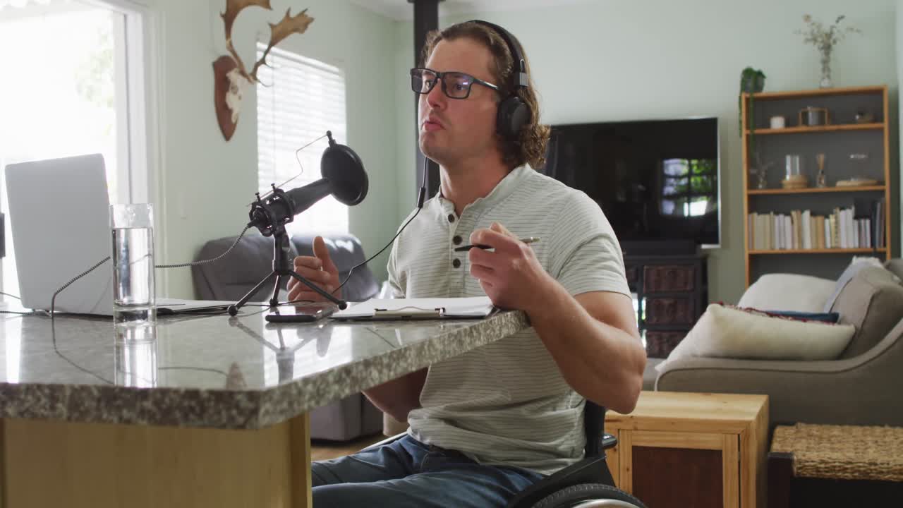 체어에 앉은 백인 장애인 남자가 헤드폰을 착용하고 녹음을 하고 메모를 하고 있습니다.