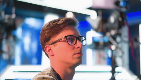 person in tv studio, focused on screen, adjusting video equipment. seen from side, studio lighting and production setup in background while working with broadcast settings