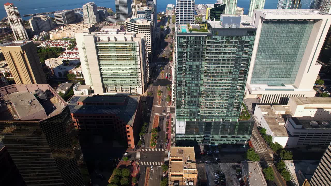 Drone voando para trás sobre o centro de San Diego às 9h da manhã, de frente para o porto, com a câmera inclinando-se lentamente para baixo para revelar as ruas abaixo
