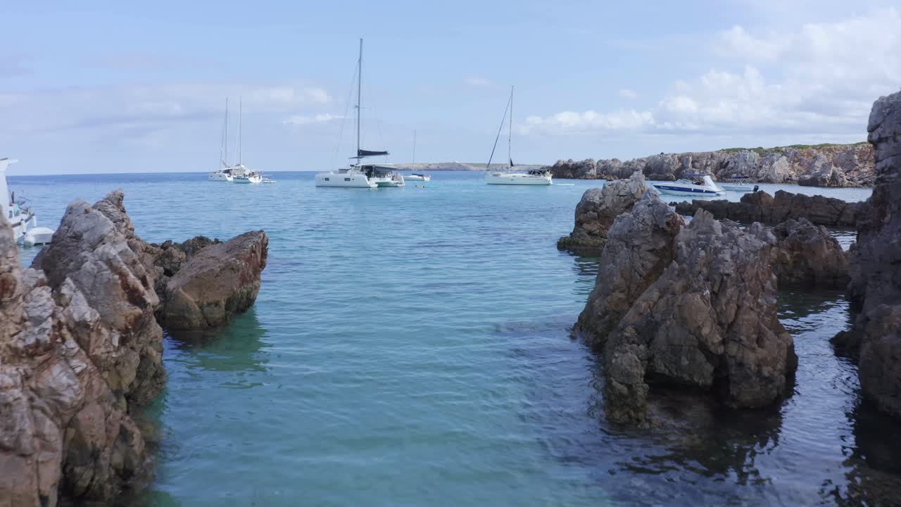 катамараны бросают якорь у скалистого побережья, когда беспилотник пролетает между скал, чтобы увидеть яхты