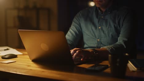 anonymous man sitting at his desk in office studio working on a laptop in the evening. man working with data, analyzing statistics. energetic fast paced movement. 360 degree tracking arc shot movement