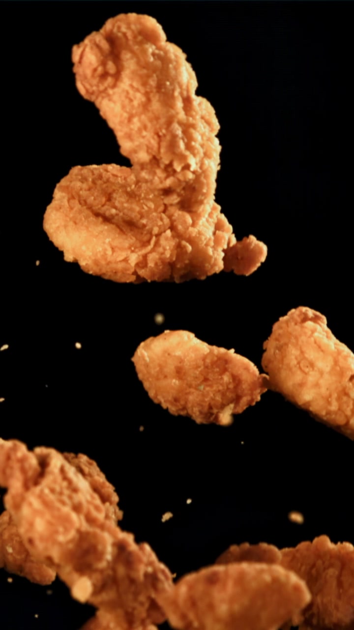 Nuggets di pollo fritti croccanti che fluttuano al rallentatore su sfondo nero