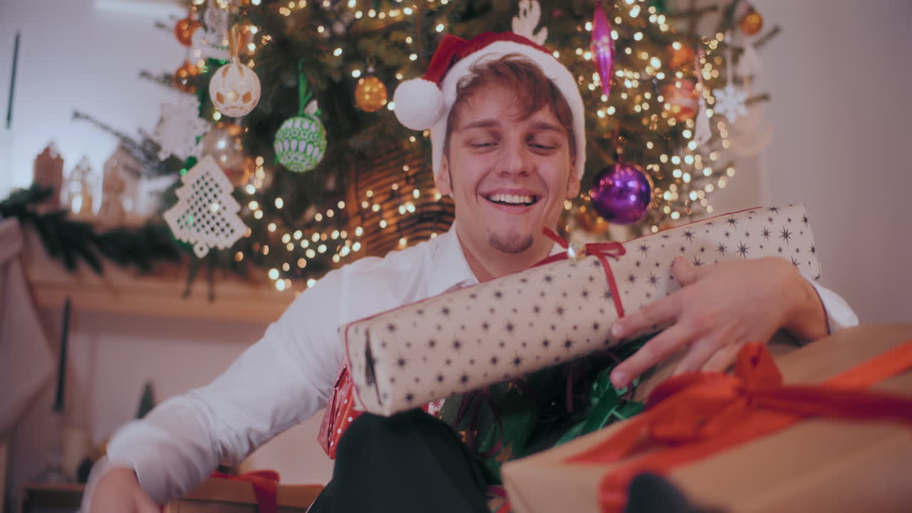 hombre emocionado con sombrero de papá noel recogiendo varios regalos de navidad envueltos
