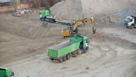 heavy machinery, including excavators and dump trucks, parked at construction site during groundwork. piles of dirt and gravel are lined up across the site, ready for transport and further processing.