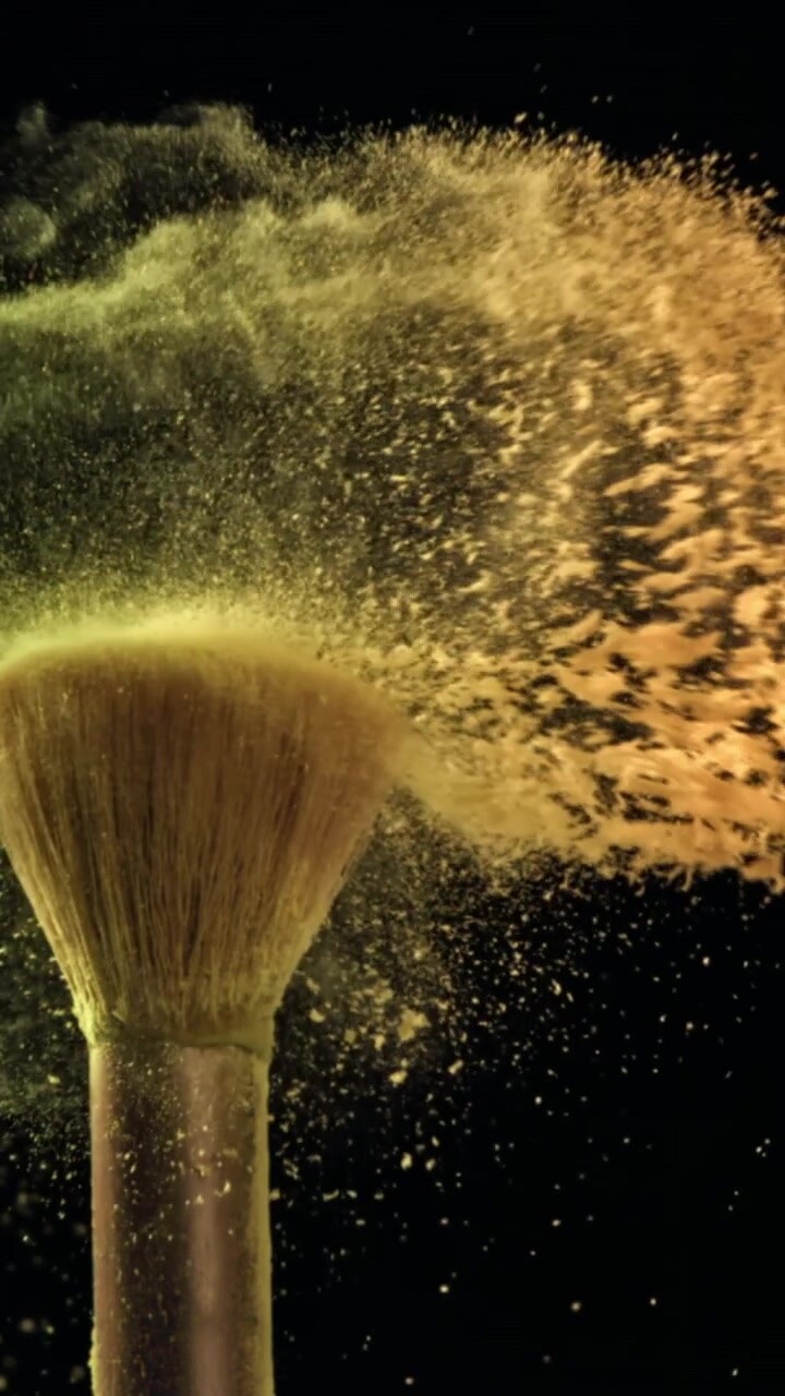 Polvere cosmetica giallo vibrante che esplode da un pennello da trucco al rallentatore