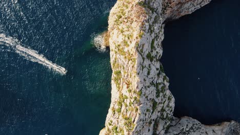 overhead shot of an electric surfer passing underneath a rocky archway off the coast of spain