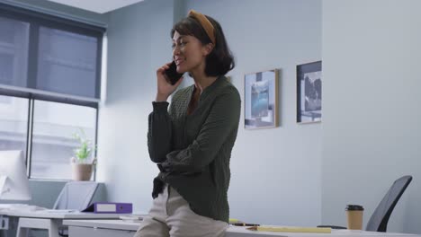 Mujer-De-Negocios-Birracial-Hablando-Por-Teléfono-Inteligente-Y-Parada-Sola-En-La-Mesa-En-La-Oficina