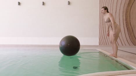 Una-Mujer-Caucásica-Salta-Y-No-Logra-Aterrizar-En-Una-Pelota-De-Ejercicio-Flotante-En-La-Piscina,-Slomo