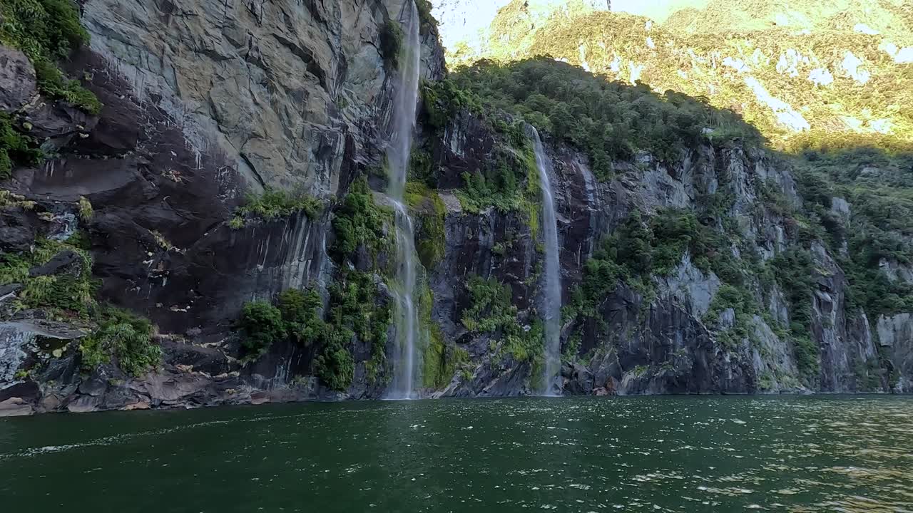 View from a boat sailing towards twin waterfalls cascading down a mountain in Milford Sound in the Fiordland National Park, New Zealand. This is a popular tourist destination in the South Island