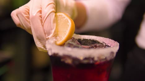 mujer con guantes blancos está poniendo limón en el borde de una copa de cóctel en un bar