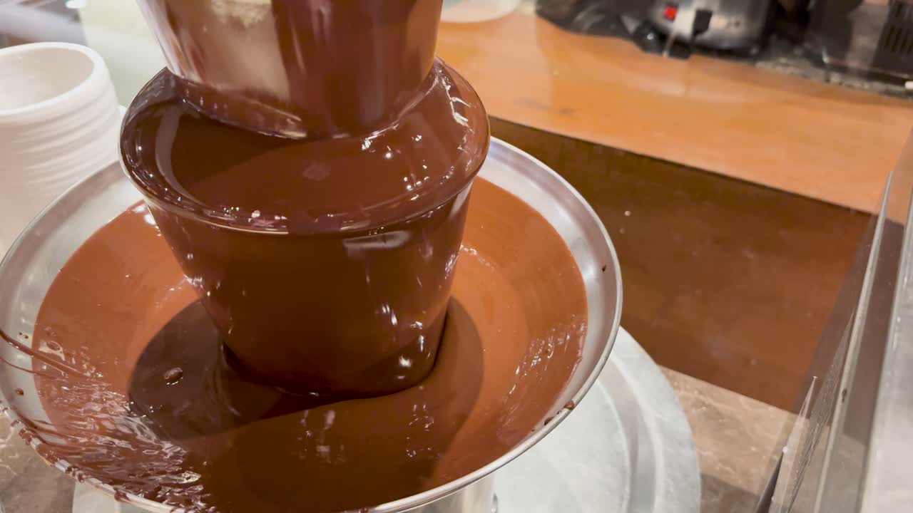A chocolate fountain flows smoothly in a buffet setting, creating a rich, indulgent atmosphere with warm lighting