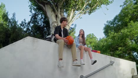 young couple sitting on a wall talking and holding a basketball