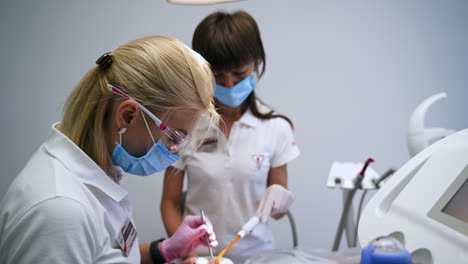 female blonde dentist taking care of dental cavity of patient. adult dark-haired nurse assisting.