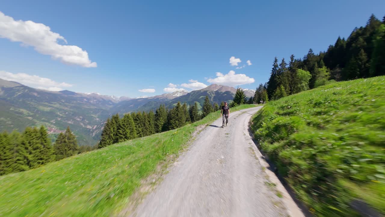 Walking Person on track of idyllic swiss alps in Switzerland. Sunny summer day in green mountains with forest trees. FPV drone speed flight.