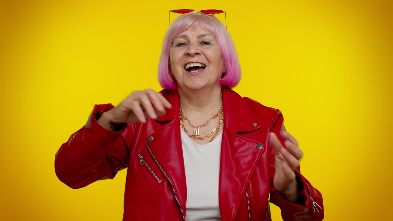 Anziana donna alla moda e positiva che si diverte a ballare, facendo dab, alzando le mani, eseguendo il gesto dubdance.