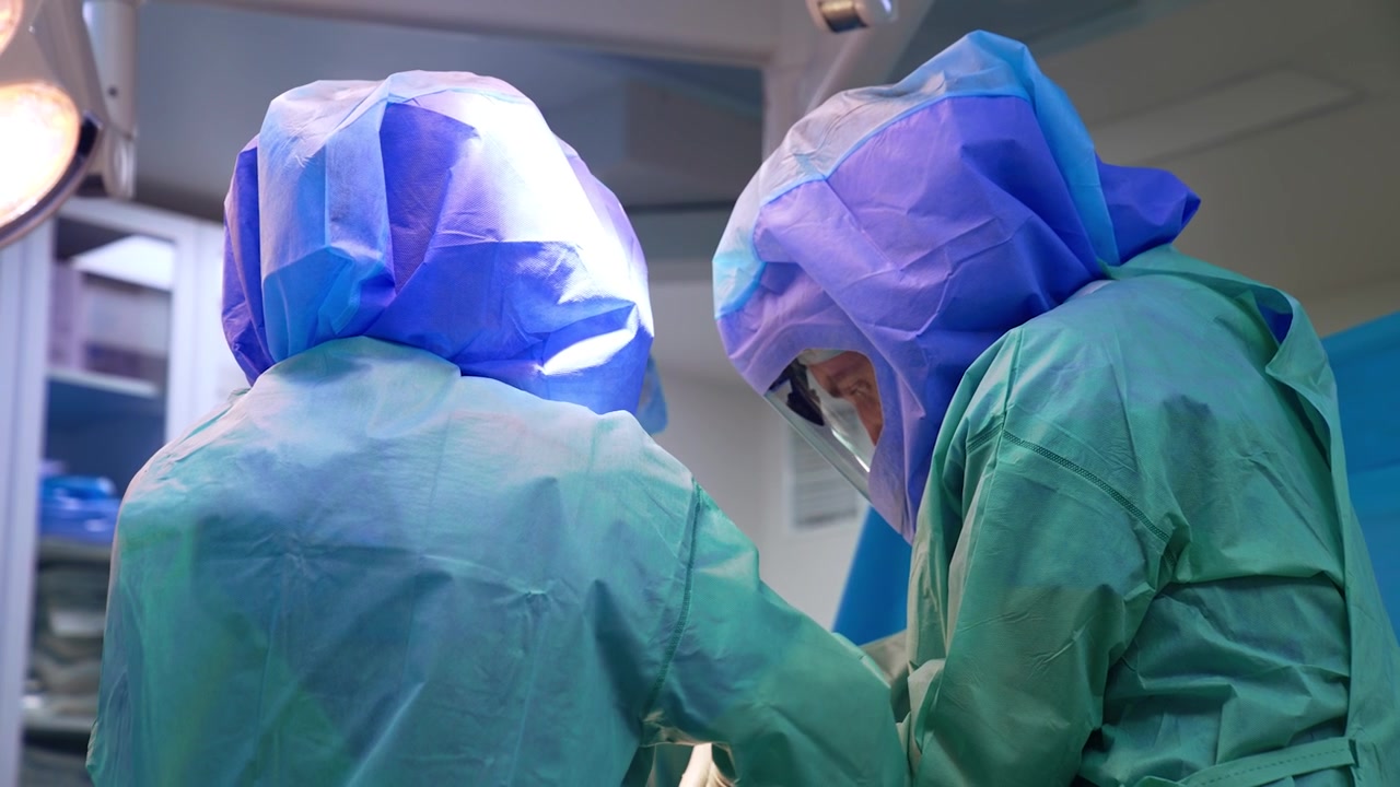 Vista posteriore di due chirurghi equipaggiati con caschi protettivi in uniformi blu. Medici che lavorano nella sala operatoria.