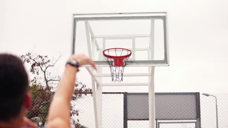 throw in a basketball hoop, the ball hits the ring and flying through the net. slow motion shot. back view of unrecognizable