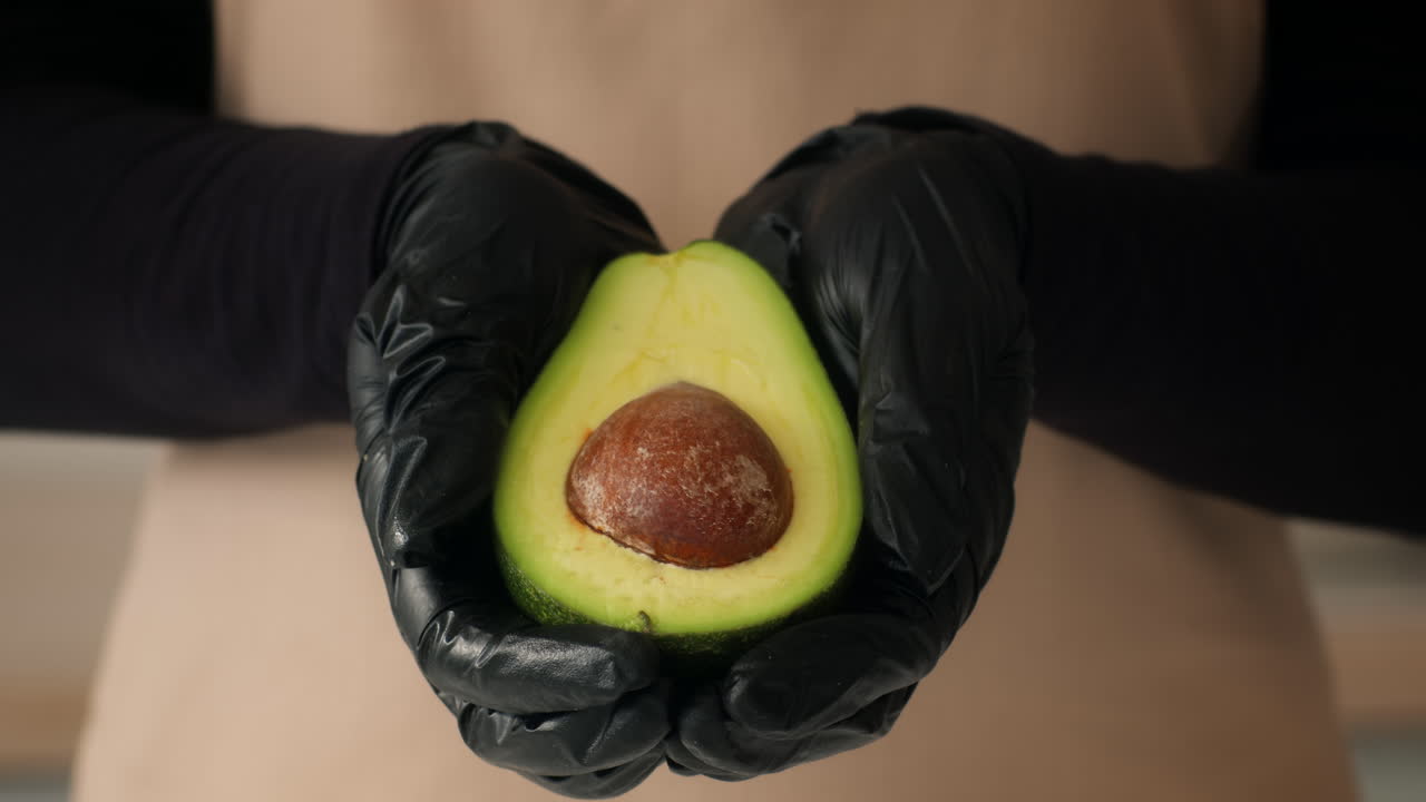 Person holding a halved avocado in black gloves