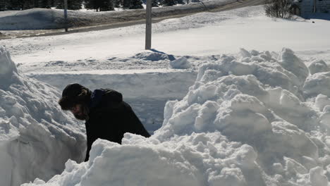 man piling snow on a snowbank on a sunny day