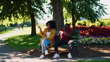 a couple enjoys a sunny day on a park bench, talking and laughing