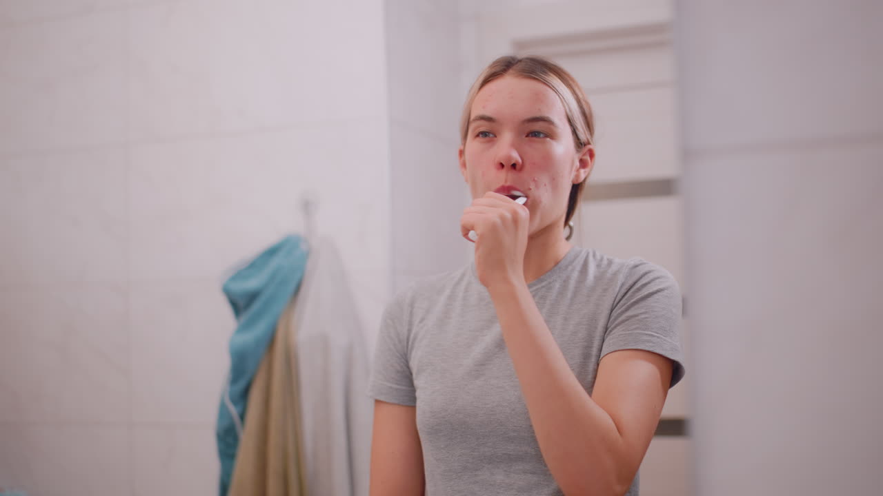 Young woman brushing teeth with toothbrush while standing in bathroom mirror, focusing on oral hygiene, dental care, morning selfcare ritual, wellness, healthy lifestyle, and personal grooming