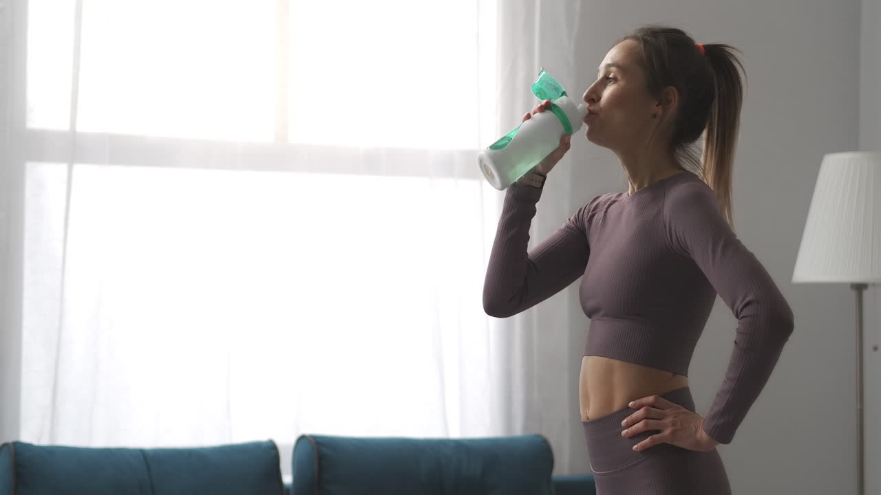 una mujer bonita con cola de caballo está bebiendo agua después de entrenar en casa relajándose y descansando después de la gimnasia estilo de vida saludable y bienestar