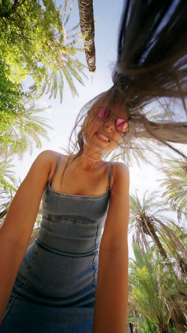 Joyful Young Woman with Hair Blowing in the Wind Under Palm Trees