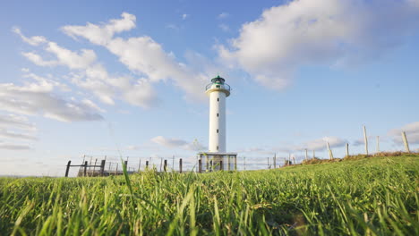 timelapse of green field with lighthouse against blue sky in pure nature and gently breeze moving grass