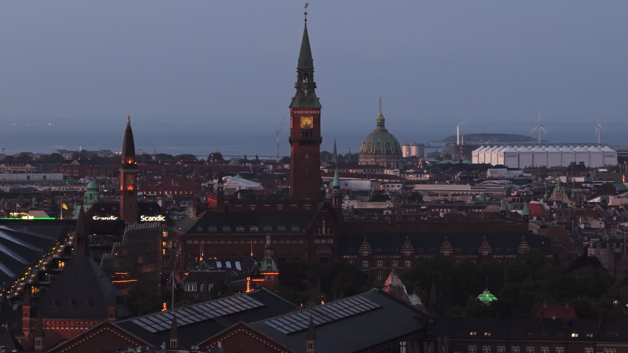 Aerial drone view of an illuminated clock tower in Radhuspladsen, with the Marble Church dome and Oresund coast visible in the background