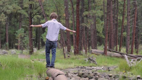 Young-man-walks-along-pipe-in-field,-steps-off,-looks-at-camera,-celebrates