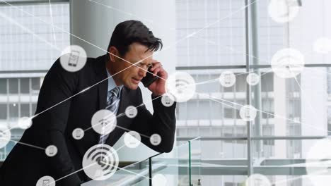 red de iconos digitales contra un hombre de negocios caucásico hablando por teléfono inteligente en la oficina