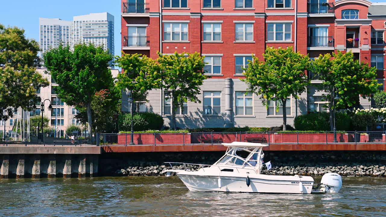New Jersey, USA, 19 August 2025: Little white motor boat goes by the river along the waterfront. Beautiful riverside of Jersey City from the waterscape